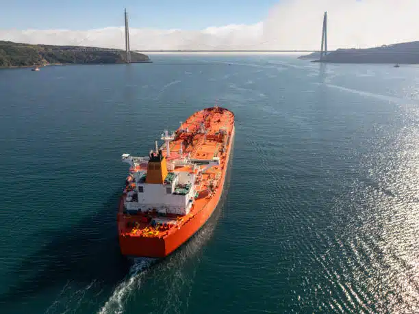 Large tanker ship navigating through a wide waterway under a bridge