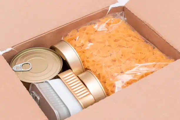 A securely packed food parcel with bow-tie pasta and canned items for safe perishable food shipping.