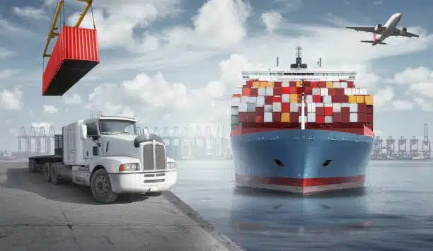 Portside scene of a container being lifted onto a drayage truck near an ocean freight ship, showing multimodal logistics in action.