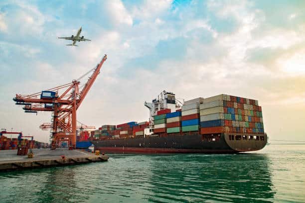 Container ship being loaded at port with airplane flying overhead, representing China to Nigeria freight services