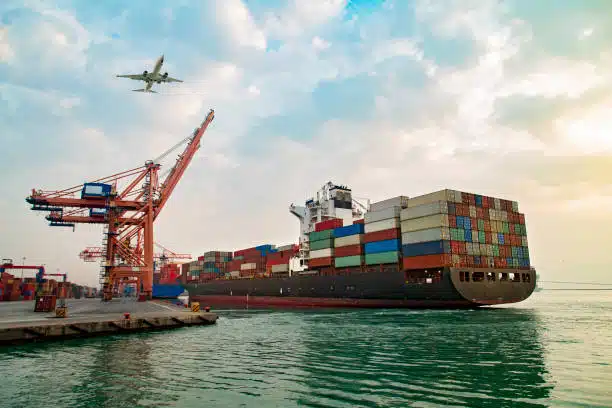 Container ship being loaded at port with airplane flying overhead, representing China to Nigeria freight services