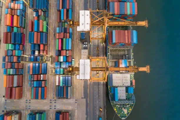 Top-down view of container yard and cargo ship loading process at shipping terminal