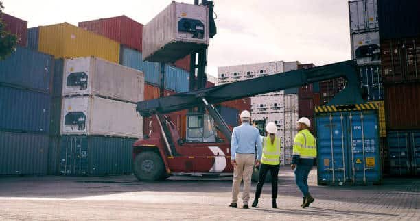 Workers supervising container loading with forklift at shipping yard