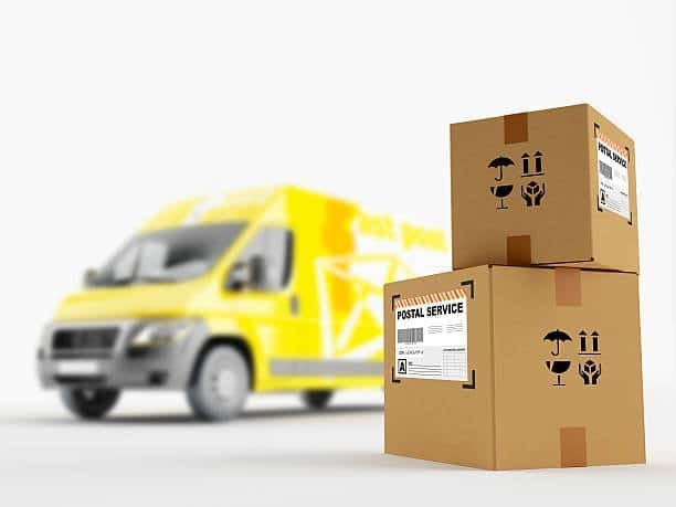 Two cardboard boxes labeled "Postal Service" in front of a yellow delivery van, representing small-parcel LTL shipments