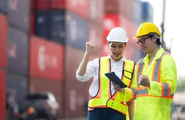 Two workers celebrating completed shipments at a port terminal, symbolizing on-time shipping performance for eBay sellers.