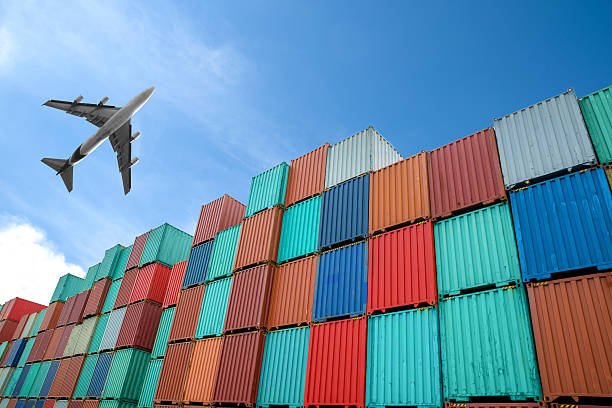 Airplane flying over stacked colorful containers at a freight terminal