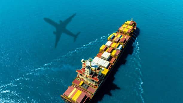 Cargo ship loaded with colorful containers and airplane flying overhead – ocean freight to Sweden