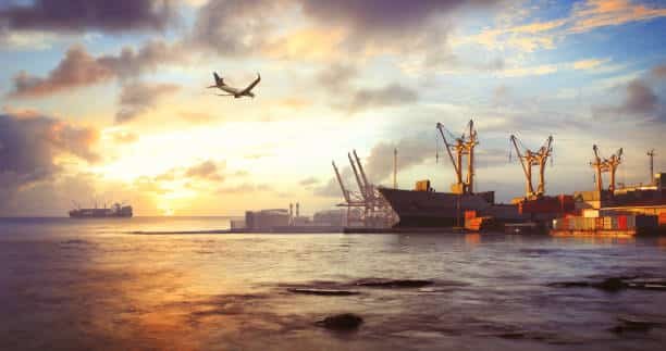 Airplane above a port at sunset, representing international shipping from China to Belgium.