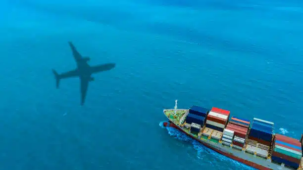 Aerial view of cargo ship with airplane shadow above, depicting air-sea logistics to Mexico.