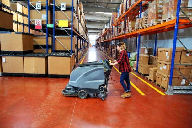 Worker using industrial floor cleaner in modern logistics warehouse