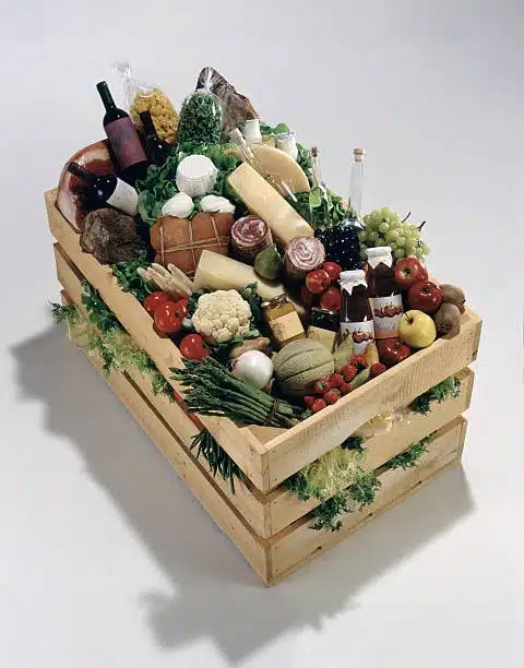 Wooden crate loaded with fresh vegetables, cheese, wine, and bottled condiments.