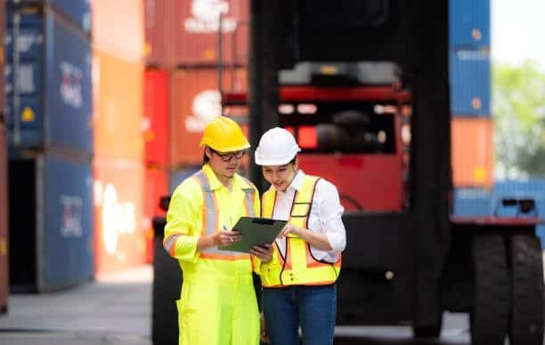 Port workers reviewing shipping documentation at freight yard