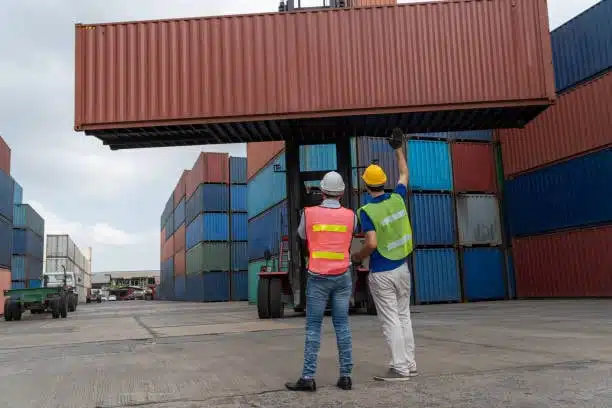 Cargo handlers directing freight container loading for shipment, highlighting seller responsibility in timely dispatch.