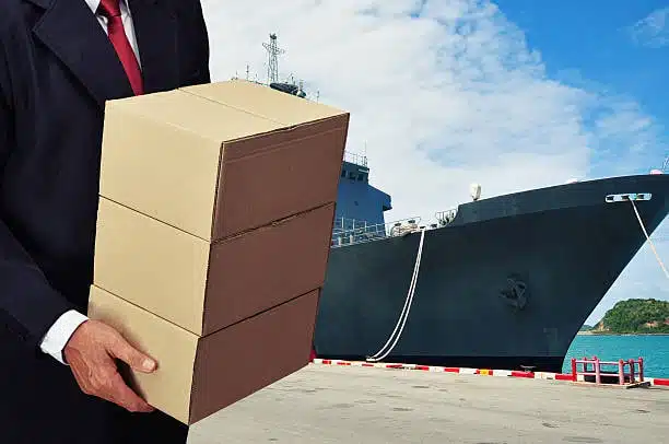 Businessman holding cargo boxes with a shipping vessel in the background