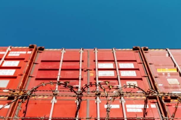 Barbed wire fence in front of stacked shipping containers