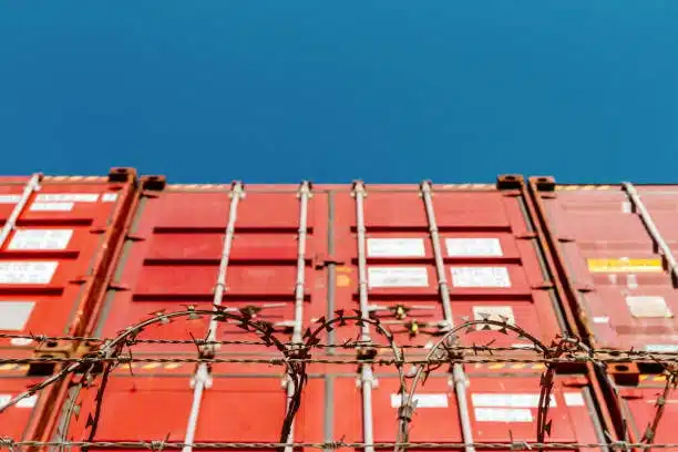 Barbed wire fence in front of stacked shipping containers