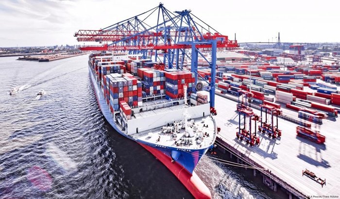 Container ship with red and blue stacked cargo units at a high-capacity European port terminal